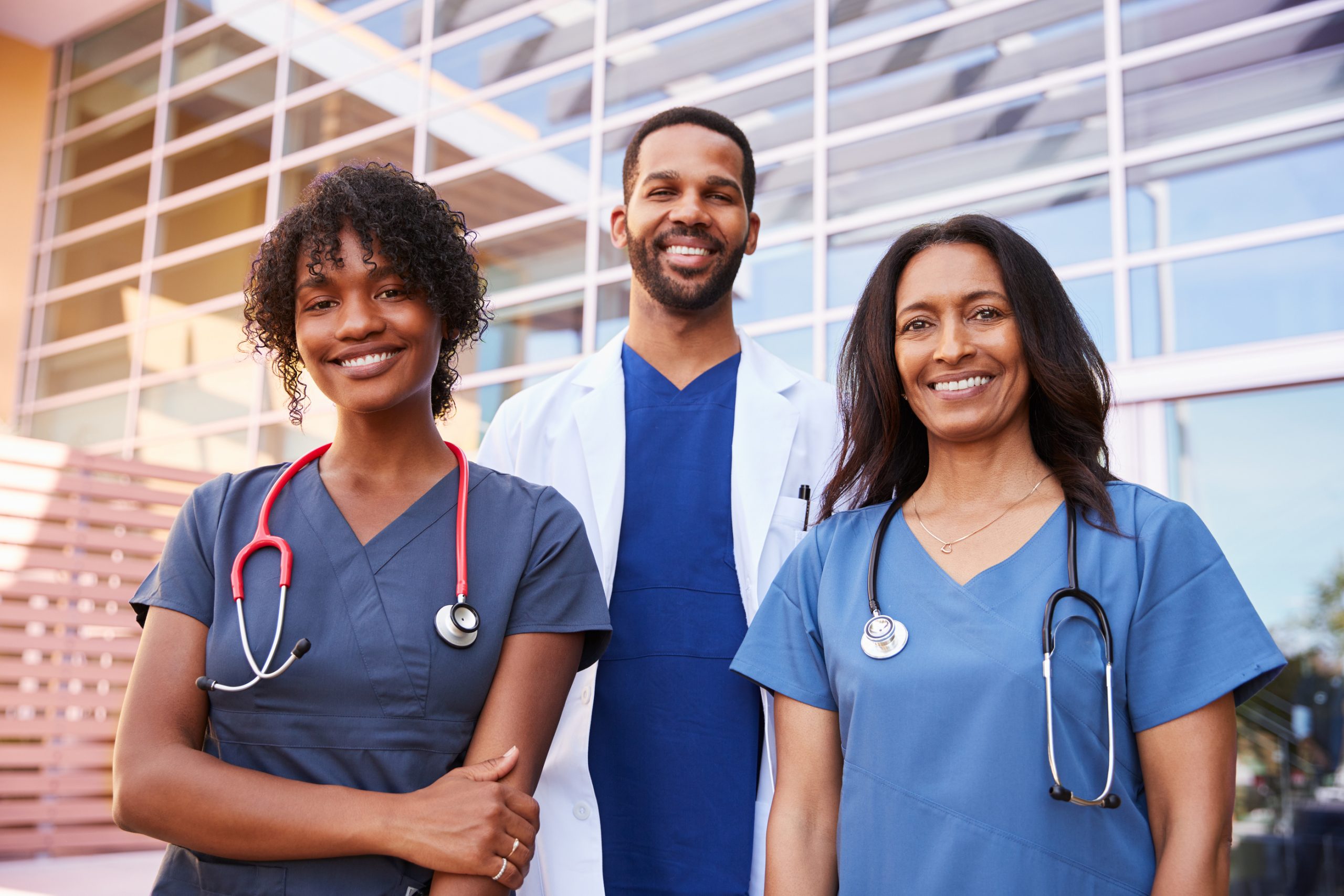 Three healthcare colleagues standing outside modern hospital Three healthcare colleagues standing outside modern hospital